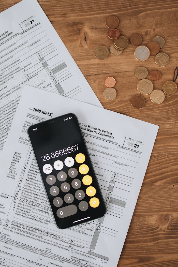 Calculator displaying number placed on tax forms with scattered coins on wooden desk.
